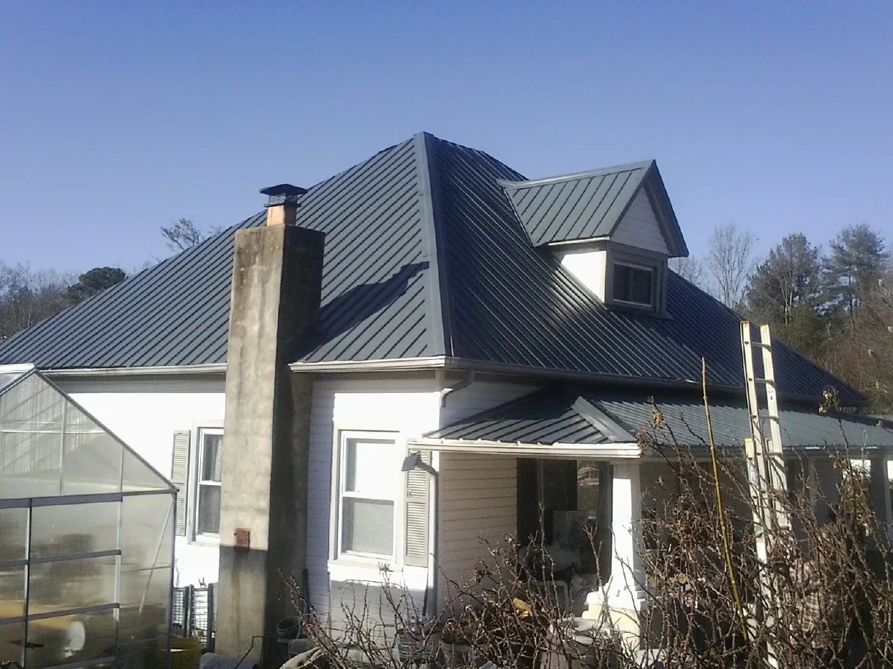 Dark blue standing seam metal roof on a white farmhouse with dormer — Slate & Tile Roof Repair by Roofing Brothers in Eckley
