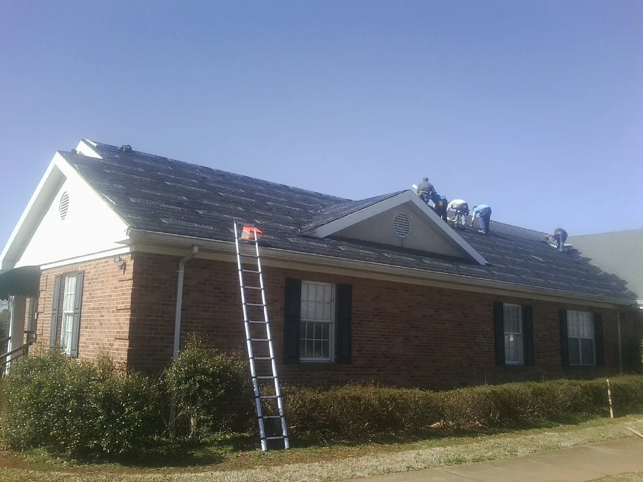 Crew tearing shingles off a brick ranch roof with a ladder set — Metal Roof Repair work by our crew in Eckley