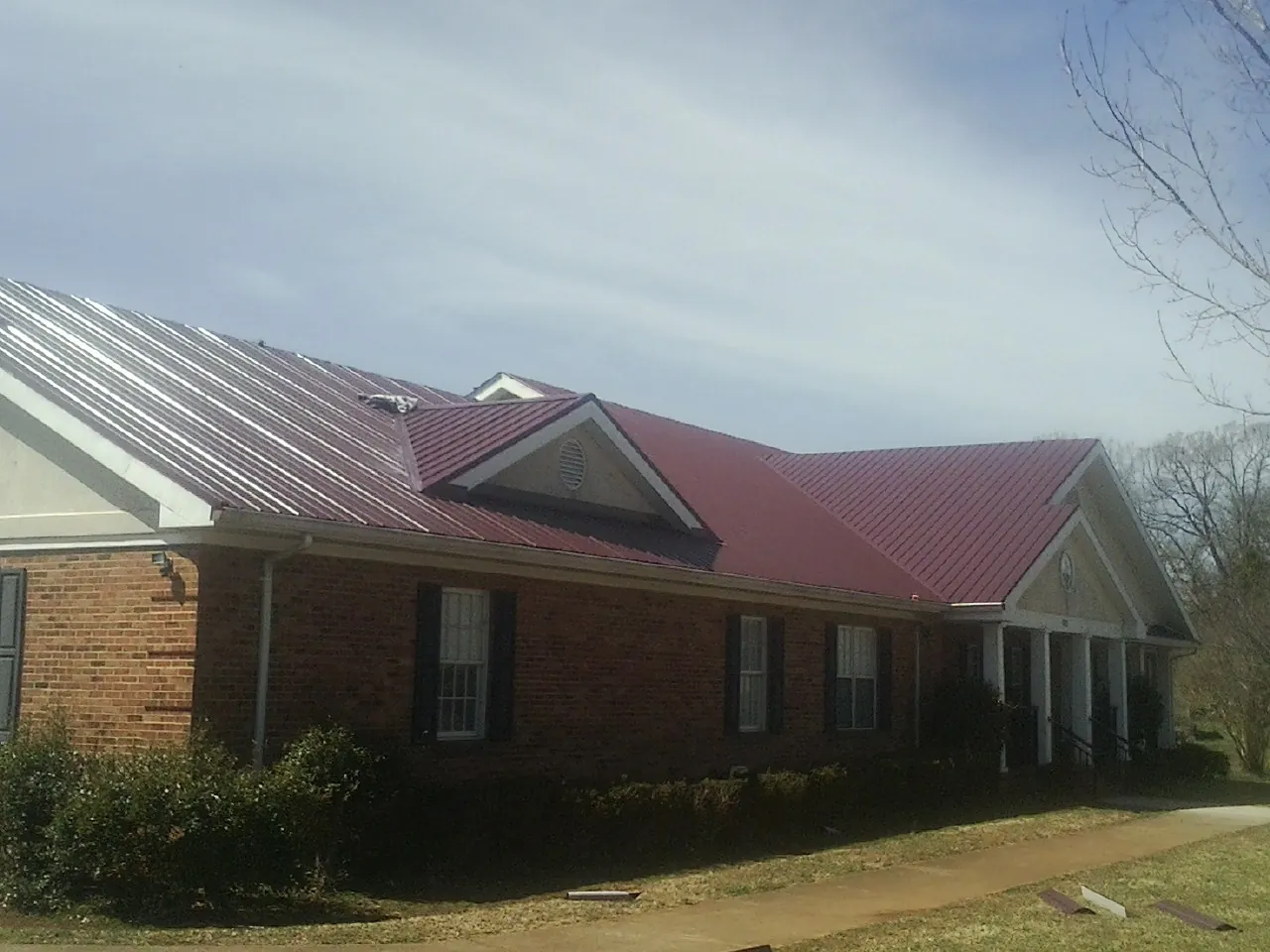 Red metal roof with gabled entries on a long brick building, from a Hail Damage Roof Repair job in Eckley