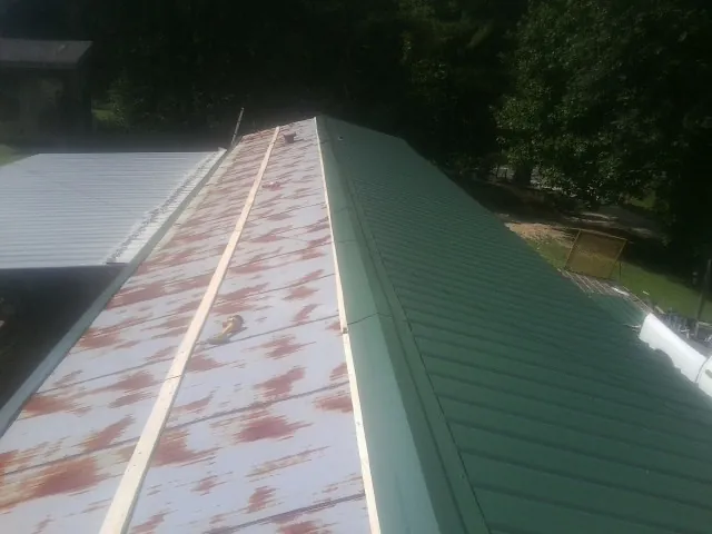 Old rusted panels beside newly installed green metal roofing — Wind Damage Roof Repair by Roofing Brothers in Eckley