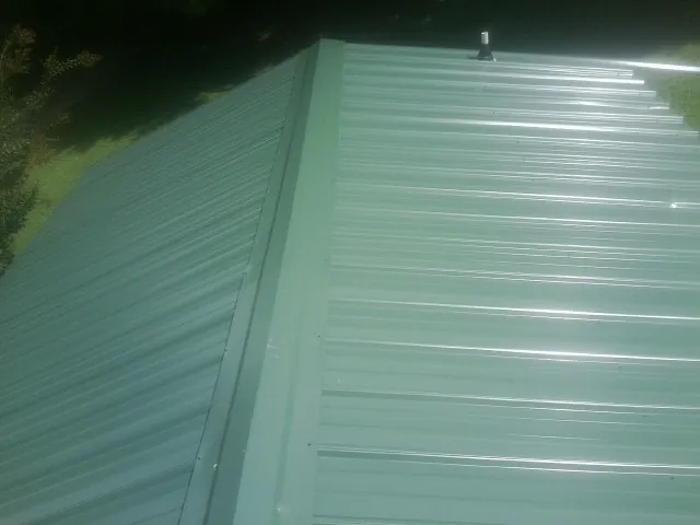 New green metal panels meeting at the ridge of a roof — Flat Roof Repair work by our crew in Eckley