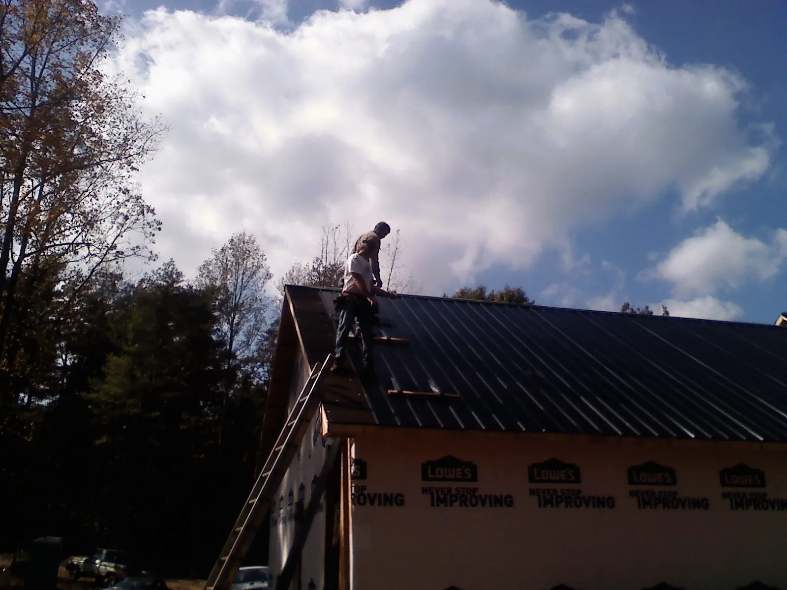 Roofer fastening dark metal panels high against a cloudy sky, from a Roof Inspection job in Eckley