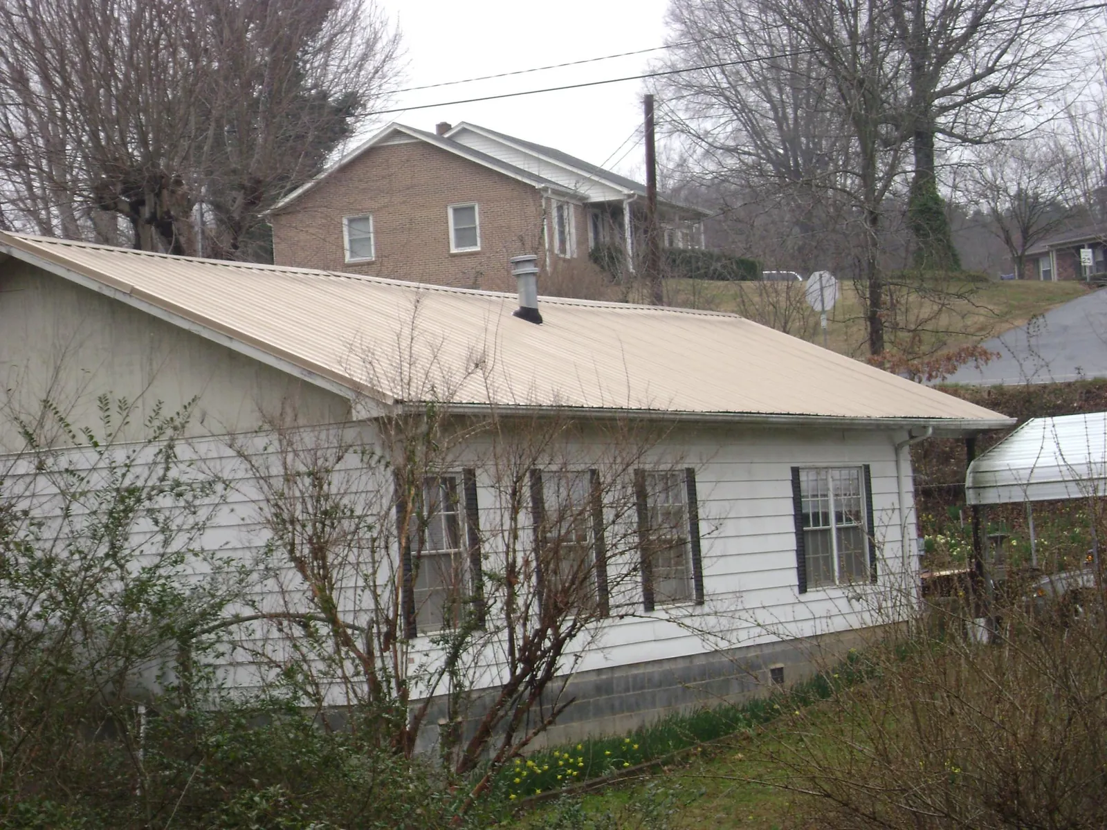 Tan metal roof on a white sided house set into a hillside — Commercial Roofing by Roofing Brothers in Eckley